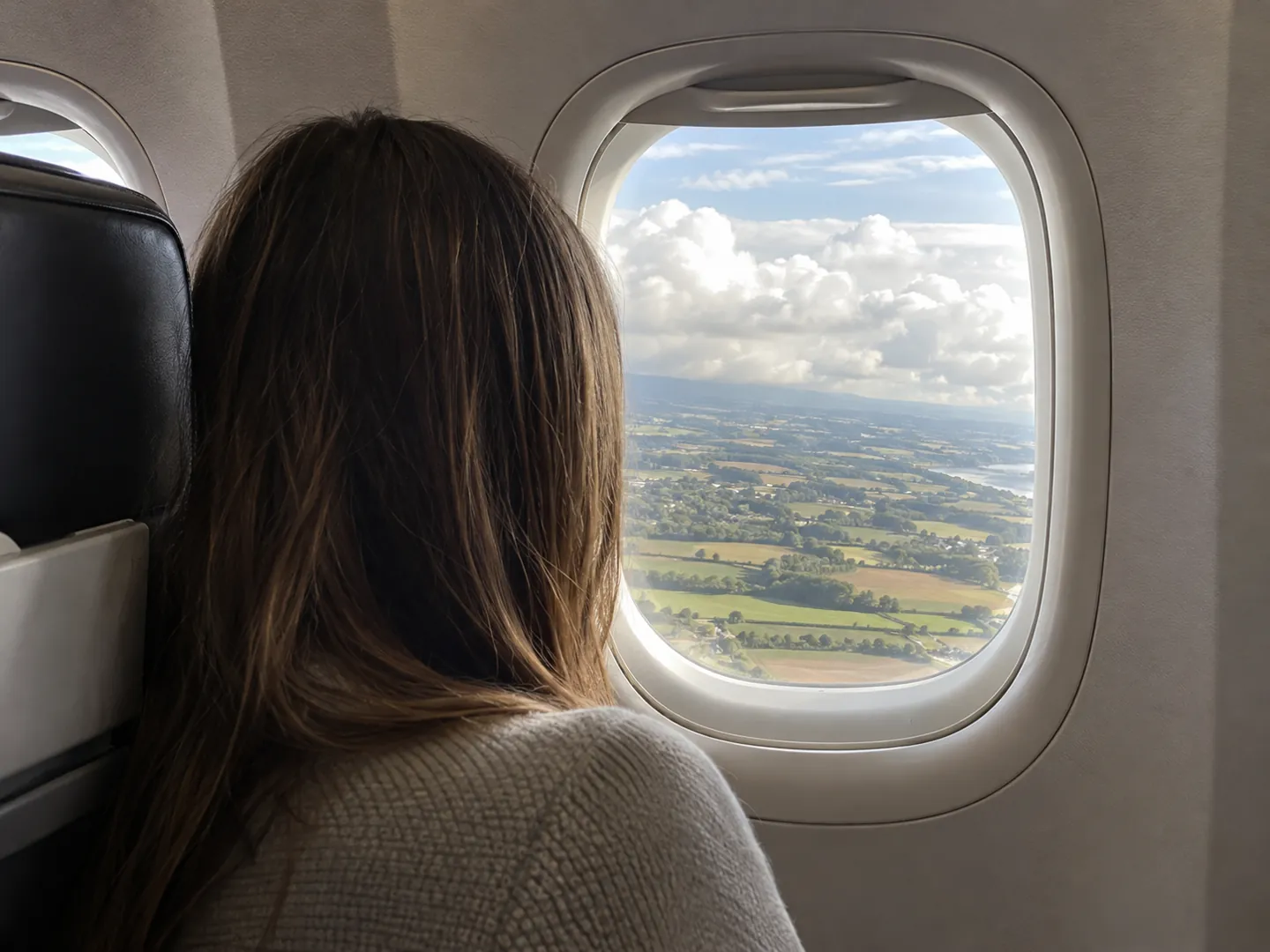 A passenger seen from behind looking out of an aeroplane window at clouds below during descent